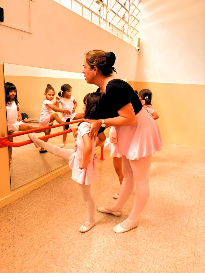 Aula de ballet com a professora corrigindo a posição das alunas na barra