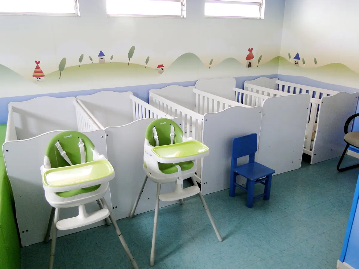 Berçário com berços, cadeirinhas de alimentação e paredes decoradas