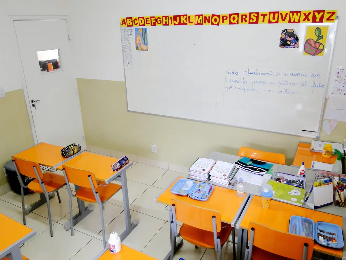 Sala do ensino fundamental com carteiras laranja, lousa e alfabeto na parede